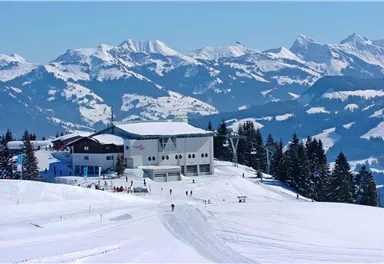 A snow-covered mountain landscape with a modern mountain lodge. In the background, majestic mountains and a clear blue sky can be seen.