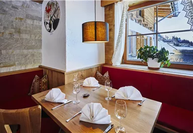 A cozy restaurant with a wooden table, nicely set and red upholstered benches. Large windows provide a view of the surroundings.