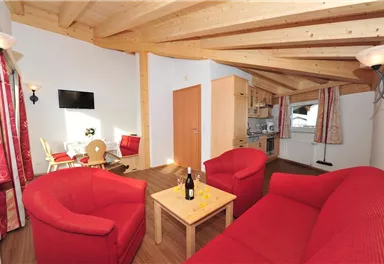 Eine helle Wohnung mit Holzdecken und rotem Sofa. Der Raum verfügt über eine Küchenzeile und einen Essbereich.