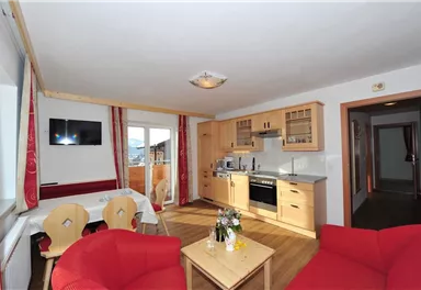 Eine gemütliche Ferienwohnung mit einer modernen Küche und einem Wohnbereich. Rote Sessel und ein Esstisch schaffen eine einladende Atmosphäre.