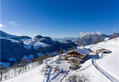 A wintry landscape with snow-covered hills and a cozy mountain cabin. The sky is clear and blue, which emphasizes the tranquil atmosphere.