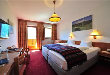 Ein gemütliches Hotelzimmer mit zwei Betten und einem Tisch. Die Fenster lassen viel Tageslicht herein und es gibt eine Aussicht auf die Berge.