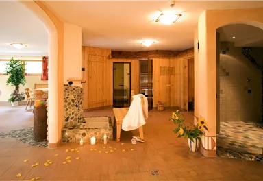 Ein entspannender Wellnessbereich mit Holzverkleidung und sanften Lichtquellen. Im Raum befinden sich Pflanzen, Kerzen und ein Zugang zur Sauna.