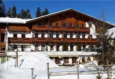 Ein charmantes Hotel im alpinen Stil, umgeben von Schnee. Die Fassade besteht aus Holz und hat Balkone mit Blick auf die Berge.