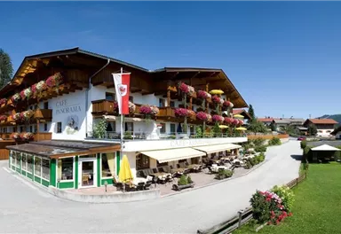 Ein gemütliches Hotel im alpinen Stil mit Balkonen, die mit Blumenkästen geschmückt sind. Umgeben von einer malerischen Landschaft und viel Grün.