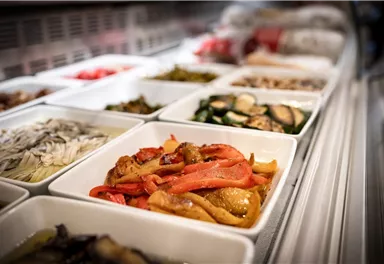 A selection of various dishes in white bowls. In the foreground, colorful bell peppers and other vegetable dishes are visible.