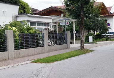 A modern building on a quiet street, surrounded by bushes and trees. The surroundings depict a well-maintained residential area with sidewalks and parking spaces.