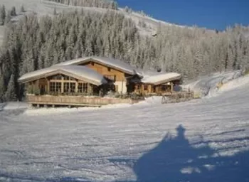 Ein gemütliches chalet in einer verschneiten Winterlandschaft. Umgeben von schneebedeckten Bäumen und klarem blauem Himmel.