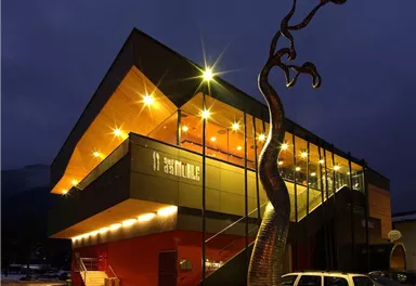 Ein modernes Gebäude mit spektakulärem Design bei Nacht. Vor der Fassade steht eine auffällige Skulptur.