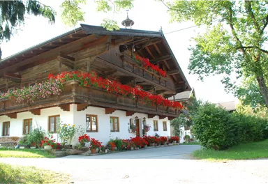 A traditional Bavarian farmhouse with wooden elements and colorful flower boxes. The entrance is surrounded by blooming plants.