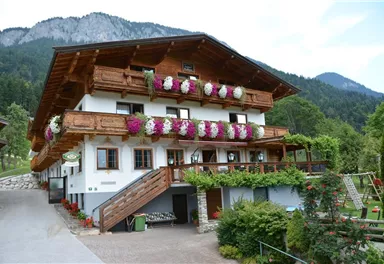 A traditional alpine house with blooming balconies. Surrounded by green mountains and an inviting garden landscape.