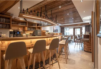 Eine gemütliche Bar mit Holzinterieur und modernen Hockern. Der Raum ist hell und einladend, ideal für gesellige Treffen.