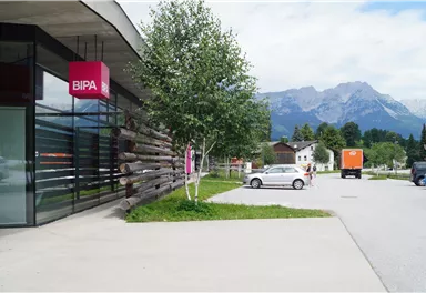 A modern store with a BIPA branch and large windows. In the background, mountains and a clear sky can be seen.
