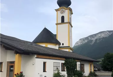 A colorful church with a tall tower and a distinctive dome. In the background, impressive mountains can be seen.