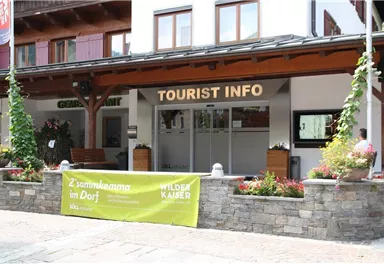 A building with the sign "TOURIST INFO" on the facade. In front of the entrance are flowers and plants in pots.