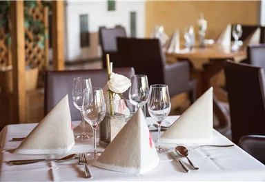 An elegant table in a restaurant, set with white napkins and glasses. In the background, more table settings are visible.