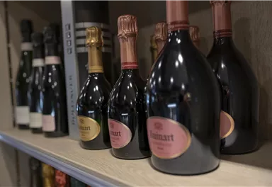 A row of champagne bottles is standing on a shelf. The bottles have different labels and colors.