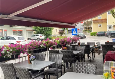 Eine gemütliche Terrasse mit rattanfarbenen Stühlen und Tischen. Bunte Blumen schmücken den Bereich und bieten eine einladende Atmosphäre.