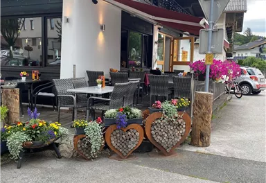 Ein gemütliches Restaurant mit einer einladenden Terrasse. Blumen und Dekorationen schaffen eine freundliche Atmosphäre.