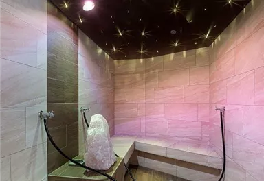 Ein moderner Dampfraum mit sanftem Licht und Holzverkleidung. An den Wänden sind ergonomische Sitzgelegenheiten und Wasseranschlüsse vorhanden.