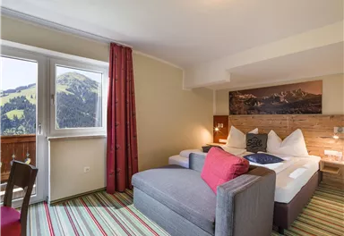 Ein gemütliches Hotelzimmer mit einem großen Bett und einem Sofa. Das Zimmer bietet einen Blick auf die Berge durch ein Fenster.