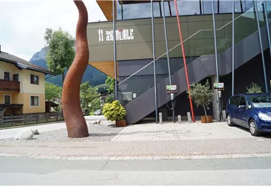 A modern designed building with an attractive sculpture in the foreground. Electric charging stations are visible on the sidewalk.