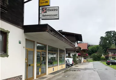 An electronics store named "Salvenmoser" on a quiet street. In the background, typical alpine buildings and a cloudy sky can be seen.