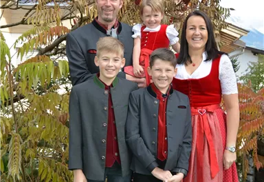 A family stands in front of a tree with colorful leaves. They all wear traditional costumes in festive colors.