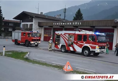Two fire trucks are standing in front of the fire station in Söll. In the background, mountains and a rural setting can be seen.