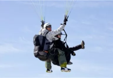 Two people paragliding in the air. They enjoy the view of the clear sky.