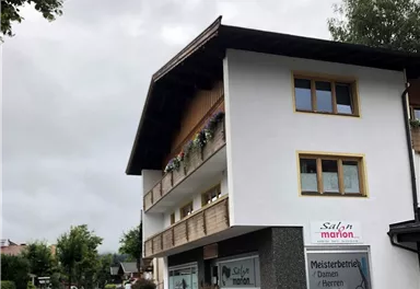 A two-story building with a hair salon and a clear street layout. Flowers are above the entrance and the sky is cloudy.