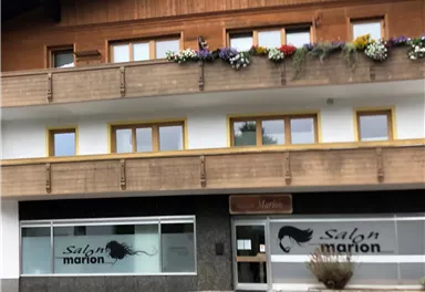 A hair salon called "Salon Marion" with large windows and a wooden building. There are flower boxes at the windows and an adjacent street.