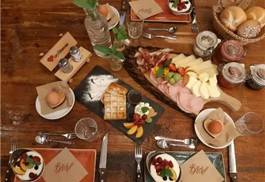 A nicely set table with various breakfast dishes. There are eggs, waffles, cold cuts, cheese, and fresh fruit.