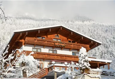 A beautiful chalet in the snow with rustic wooden elements. The snowy landscape and the mountains in the background create an idyllic winter atmosphere.