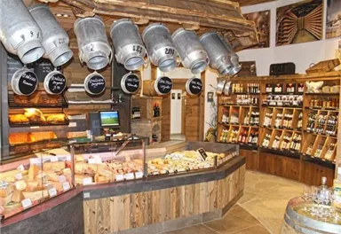 Ein gemütlicher Laden mit einer Auswahl an Käse und Wein. Die Wände sind aus Holz und das Ambiente ist rustikal und einladend.