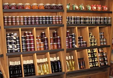 Eine Holzregal mit verschiedenen Gläsern und Flaschen. Die Produkte umfassen Marmeladen, Öle und Saucen in unterschiedlichen Farben und Größen.