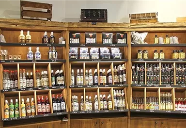 Ein Holzregal mit verschiedenen Flaschen von Likören und Essenzen. Die Produkte sind ordentlich angeordnet und gut sichtbar.