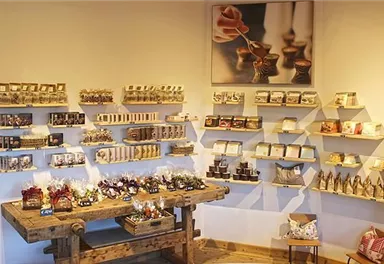 Ein stilvoller Verkaufsraum mit Regalen voller handgefertigter Produkte. Auf einem Holztisch sind verschiedene Geschenke und Dekorationen ausgestellt.