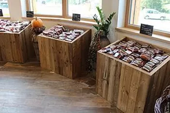 Drei Holzkisten mit verschiedenen Süßigkeiten stehen in einem hellen Raum. Fenster mit Blick nach draußen lassen viel Licht herein.