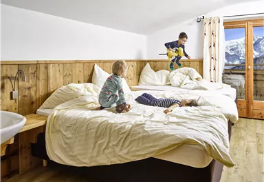 A cozy sleeping room with two large beds and a wooden wall. Three children are playing on the beds and enjoying the relaxed atmosphere.