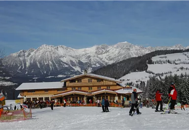An alpine ski landscape with a cozy chalet and snow-covered mountains in the background. Skiers and visitors enjoy the winter weather.