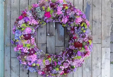 A beautiful flower crown in various shades of purple and green. It is richly adorned with roses and other colorful flowers.