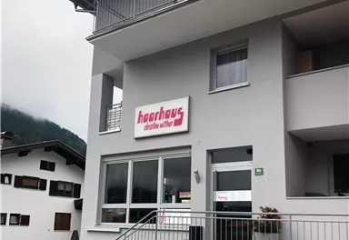 A modern building with a clear, minimalist design. In front of the entrance is a sign with the name "Haarhaus".