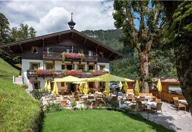 Ein gemütliches Restaurant in den Bergen mit einer einladenden Terrasse. Gelbe Sonnenschirme und Blumen schmücken die Außenbereiche.