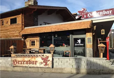 A rustic building with a wood design known as the Witch Bar. The facade features a sign and some decorative lanterns.