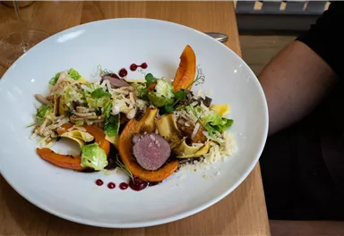 An artistically arranged plate with vegetables and meat, garnished with fresh salad. The colors are vibrant and appealing.