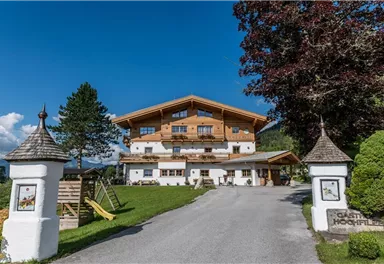 A picturesque Alpine house with wooden cladding and a beautiful garden. In the foreground, a paved driveway leads to the front door.