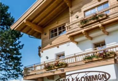 An inviting wooden house with a "Welcome" sign in the foreground. In the background, there is a green landscape and a blue sky.