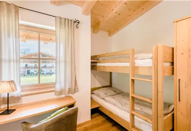 A cozy bedroom with a bunk bed and a desk. Bright curtains next to the window create a friendly atmosphere.