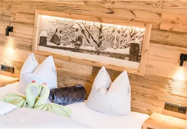 A cozy bedroom with wood paneling and comfortable pillows. In the background, there is a decorative picture of a winter landscape.